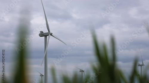 Group Of Wind Turbines Spinning With Blurred Grass In The Foreground