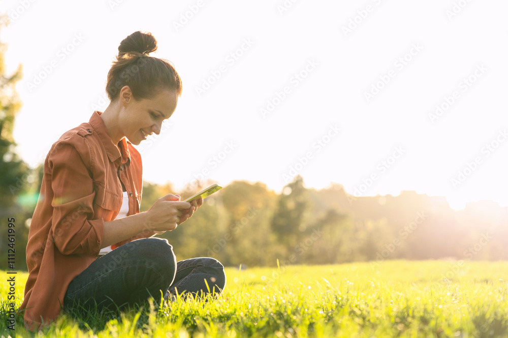 Caucasian woman sitting on green grass in a city park, texting on her smartphone. Caucasian woman sitting on green grass in a city park, texting on her smartphone.