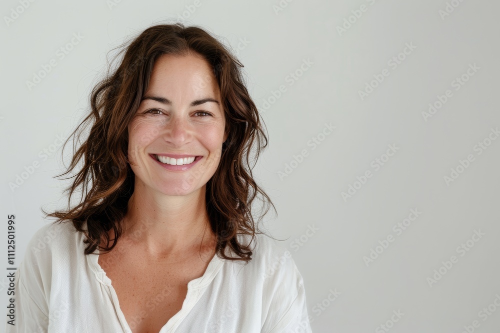 Portrait of a smiling caucasian woman in her 40s wearing a simple cotton shirt while standing against white background Portrait of a smiling caucasian woman in her 40s wearing a simple cotton shirt while standing against white background