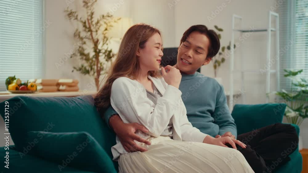 Young asian couple enjoying each other's company, cuddling and laughing together on a cozy sofa in their living room, radiating warmth and affection in a relaxed atmosphere Young asian couple enjoying each other's company, cuddling and laughing together on a cozy sofa in their living room, radiating warmth and affection in a relaxed atmosphere