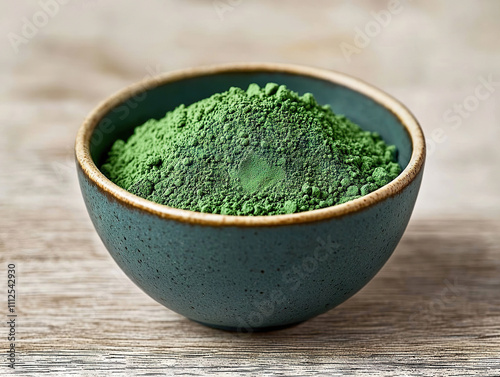 Green powder in bowl on wooden surface, showcasing its vibrant color and texture, perfect for culinary or health related themes photo