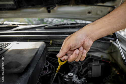 A man's hand pulls the oil dipstick to check the oil level and maintain the car. Close-up of mechanic's hands pulling oil dipstick inside engine compartment.