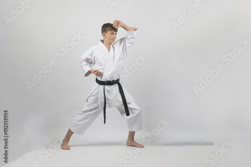 Fifteen year old male teenage karate black belt in long stance doing a head block, studio shot against a white background