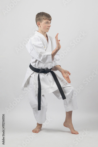 Fifteen year old male teenage karate black belt in a cat stance with open hand block, studio shot against a white background photo