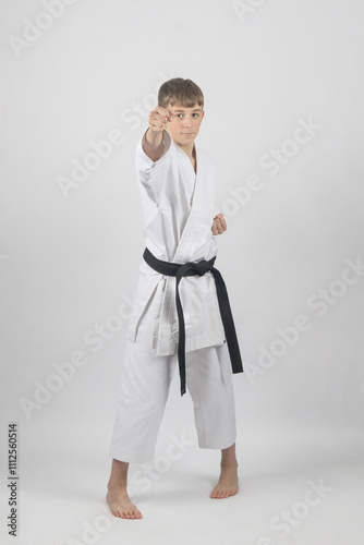 Fifteen year old male teenage karate black bel in sanchin stance doing a back fist , studio shot against a white background