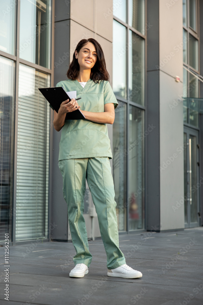 Dark-haired young female doctor near the clinic with a prescription list in hands