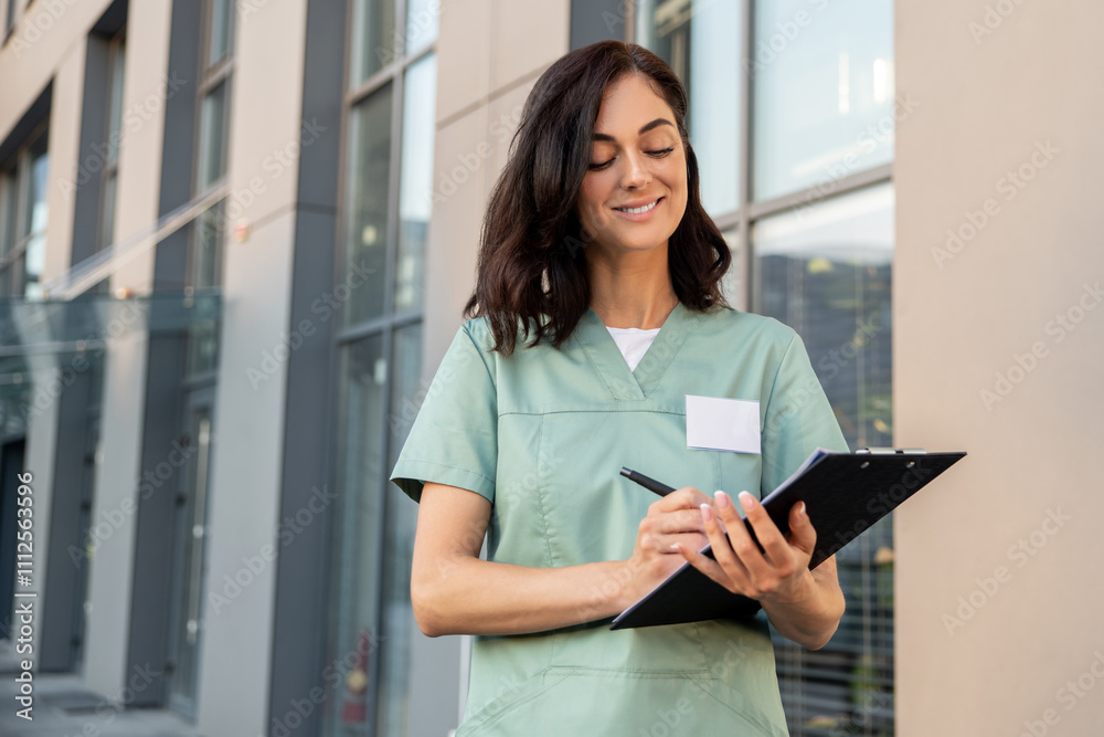 Fototapeta premium Dark-haired young female doctor near the clinic with a prescription list in hands
