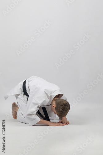 Fifteen year old male teenage karate black belt bowing, studio shot against a white background