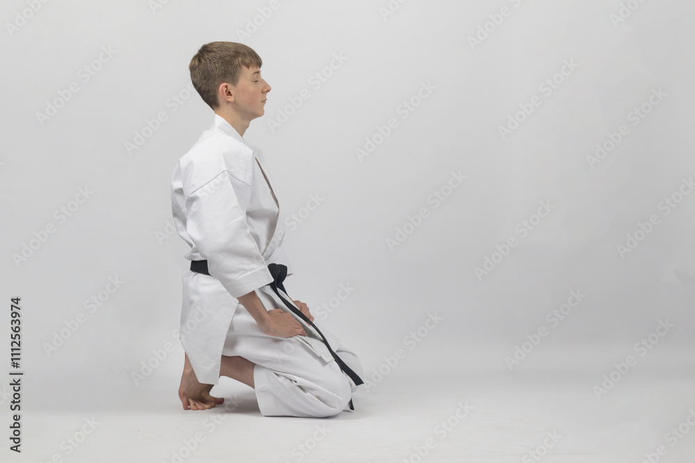 Obraz premium Fifteen year old male teenage karate black belt kneeling eyes closed, studio shot against a white background