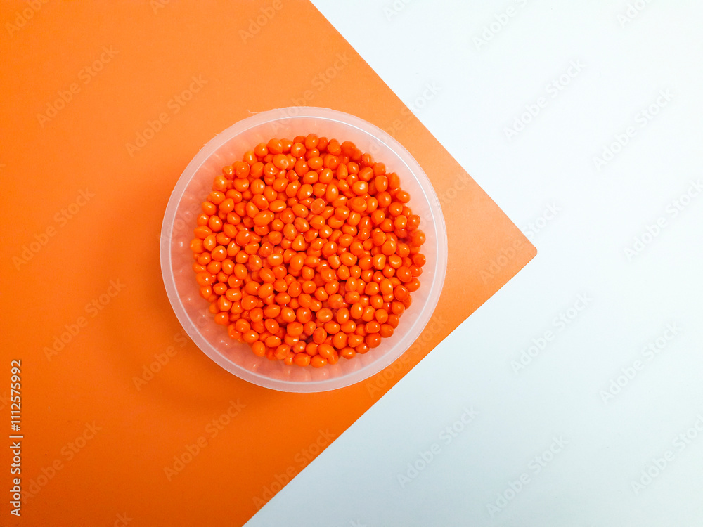 Orange masterbatch granules in plastic cup on white and orange background,color pigment carrier polymer in plastic industry.Suitable for plastic company catalog design Orange masterbatch granules in plastic cup on white and orange background,color pigment carrier polymer in plastic industry.Suitable for plastic company catalog design
