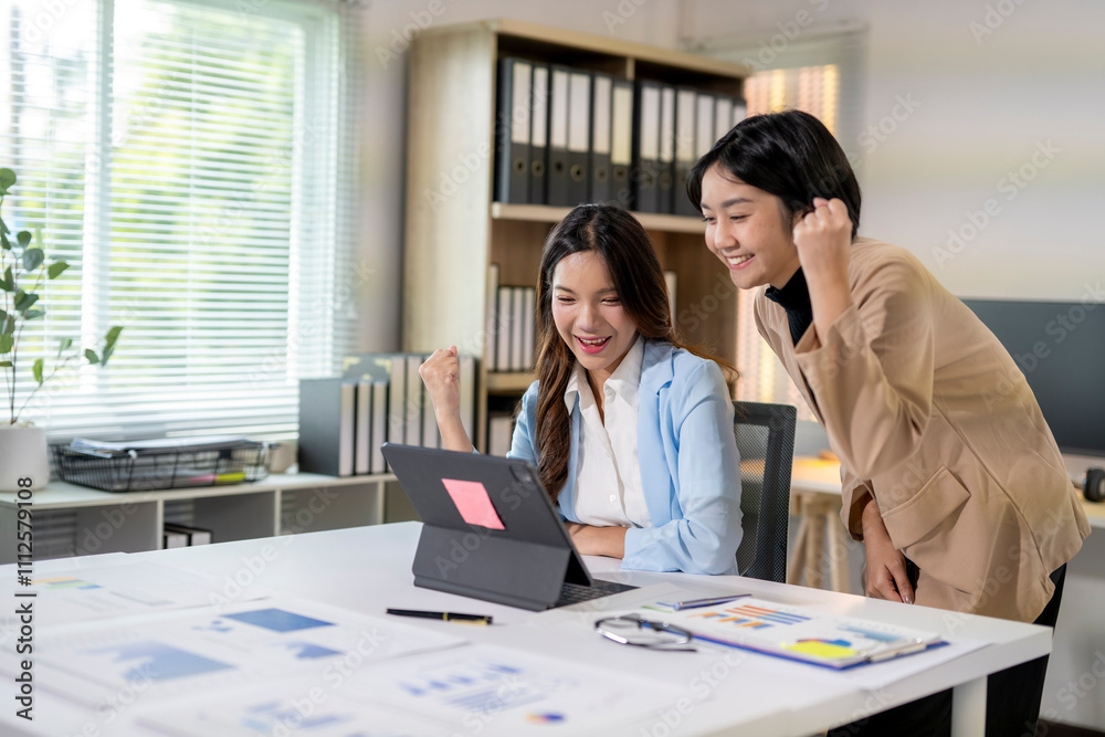 Two businesswomen celebrating success while looking at tablet in office Two businesswomen celebrating success while looking at tablet in office