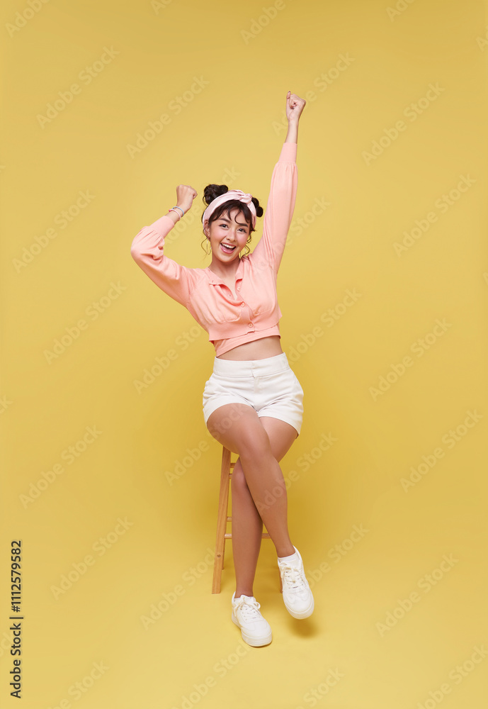 Attractive beautiful Asian teen woman sitting on chair and hands up raised arms success celebration.