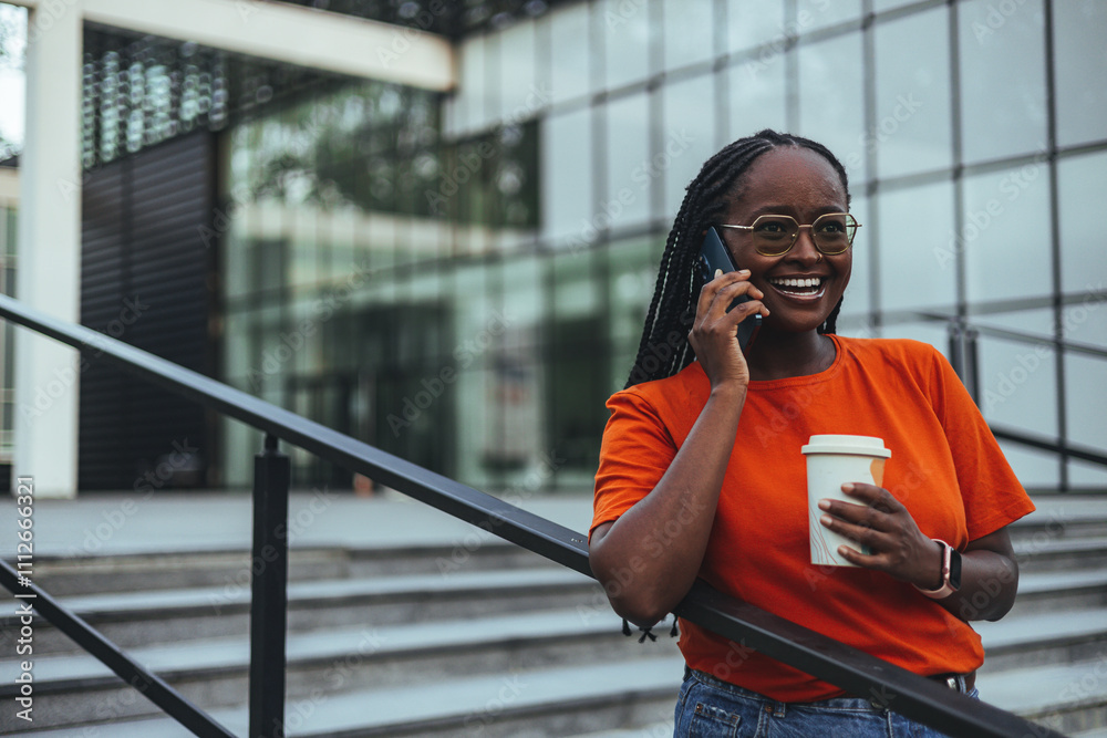 Fototapeta premium Smiling Woman Talking on Smartphone While Holding Coffee Cup Outdoors