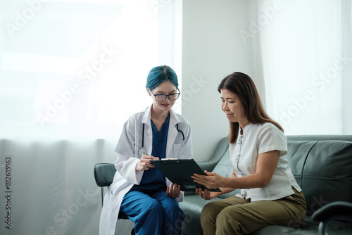 A woman and a doctor are sitting on a couch, looking at a clipboard