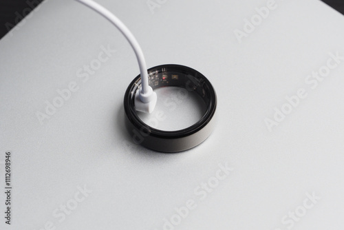 Smart ring is connected to a charging cable resting on a minimalist surface, illustrating advancements in wearable technology and modern design.