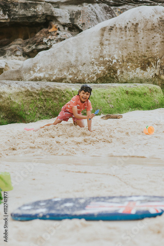 A young boy wearing a legionnaire hat and swim dress is playing with the sand using a yellow bucket at Tamarama Beach in Sydney