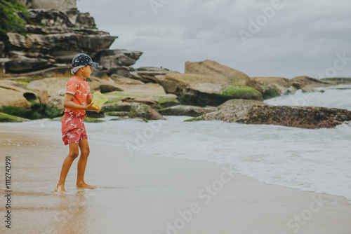 A young boy wearing a legionnaire hat and swim dress is playing with the sand using a yellow bucket at Tamarama Beach in Sydney photo