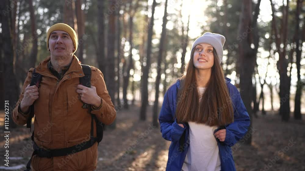 a couple of tourists are walking through the forest. forest tourism concept. happy young lifestyle couple walking through the spring forest with backpacks and sun glare. tourist a couple of tourists are walking through the forest. forest tourism concept. happy young lifestyle couple walking through the spring forest with backpacks and sun glare. tourist