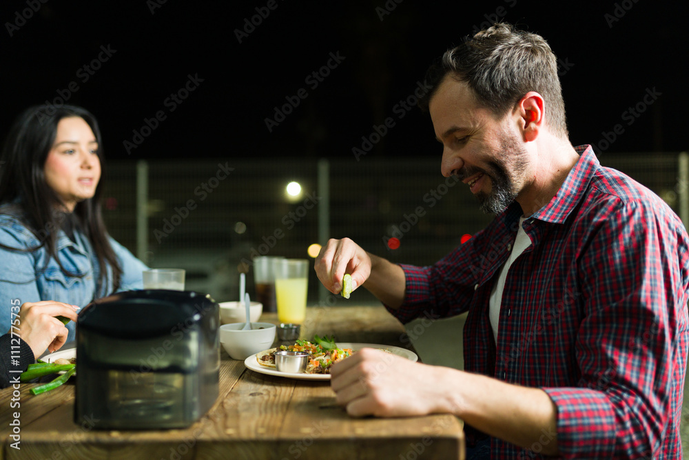 Happy man adding lime to tasty tacos during nighttime dinner with friends at a mexican taco stand outdoors Happy man adding lime to tasty tacos during nighttime dinner with friends at a mexican taco stand outdoors