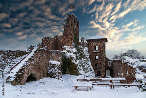 A castle with a snow covered roof and a steeple. The castle is surrounded by a snowy landscape. Ruin of Hohnstein Castle, Harz mountains, Germany.