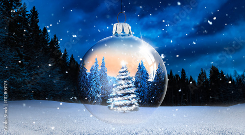 Gläserne Weihnachtskugel vor verschneitem Winterwald