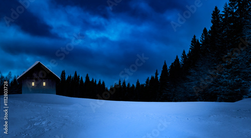 Gemütliches Cottages mit beleuchtetem Fenster in verschneitem Winterwald