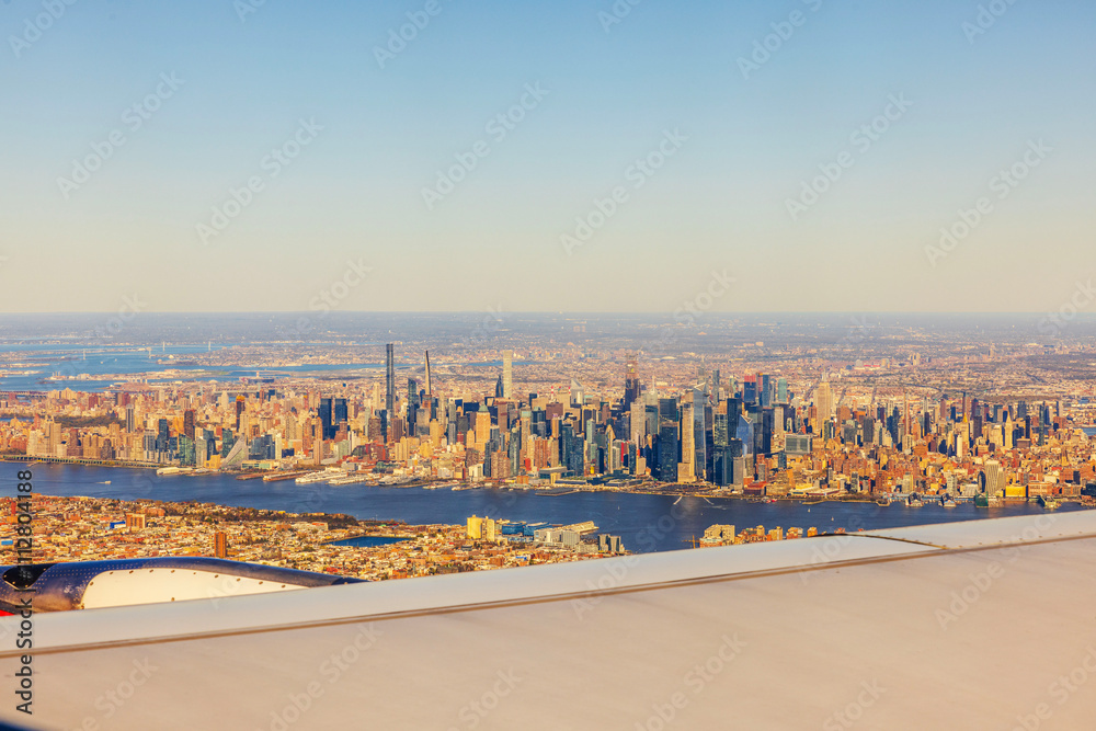 Obraz premium Aerial view of Manhattan skyline with Hudson River and iconic skyscrapers during golden hour from airplane window in flight. USA.