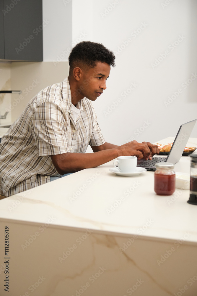 Young black man working on laptop at kitchen table Young black man working on laptop at kitchen table