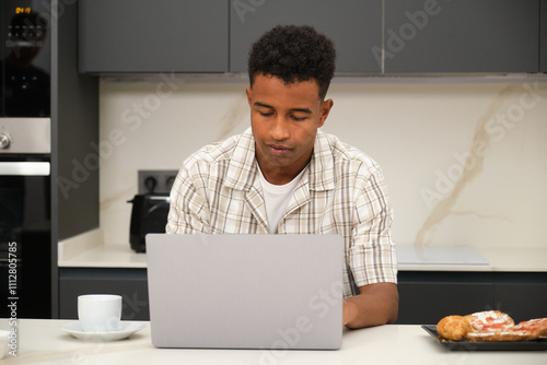 Young African American Man Using Laptop in Modern Kitchen photo