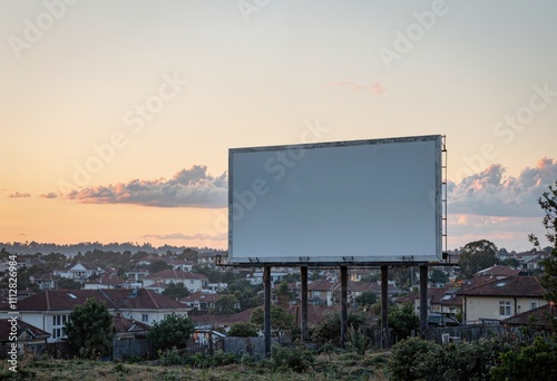 Blank billboard in suburban landscape at sunset with houses and trees in the background. Outdoor advertising concept with copy space for design and print. photo