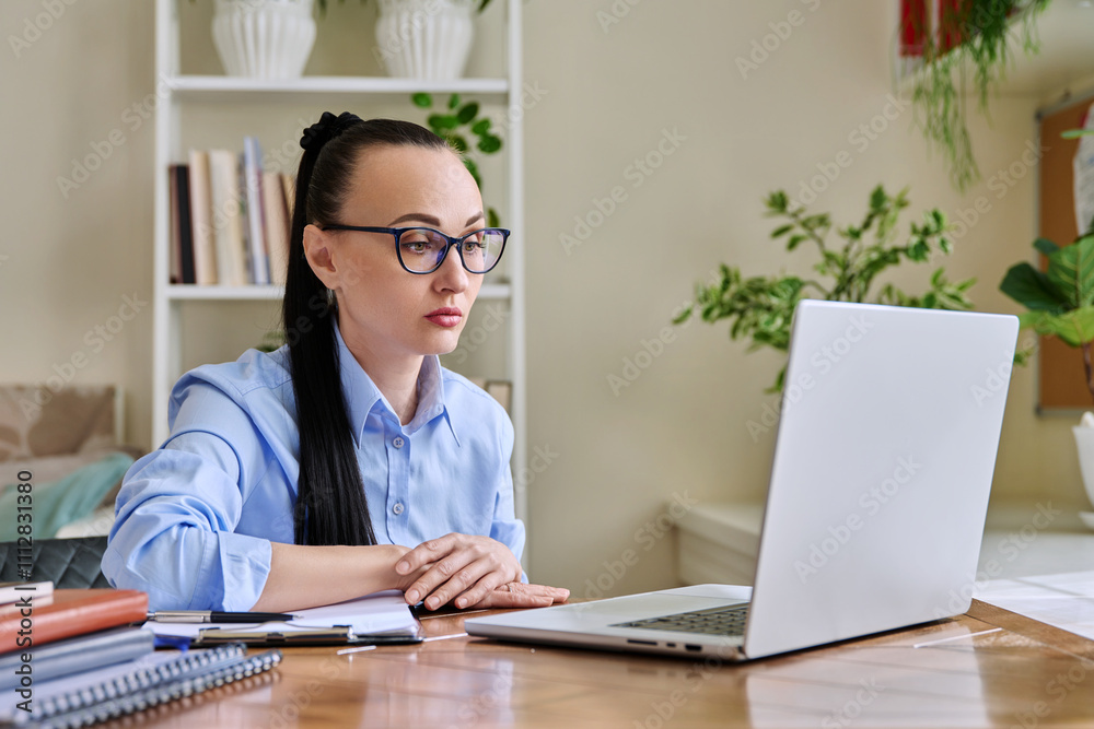 Middle-aged woman working at computer, looking at web cam talking, in home office Middle-aged woman working at computer, looking at web cam talking, in home office