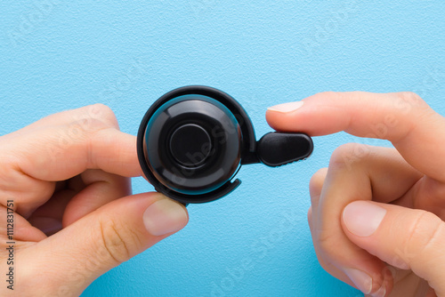Young adult woman hands holding and showing new black dark bicycle bell on light blue table background. Pastel color. Closeup. Point of view shot. Top down view. photo