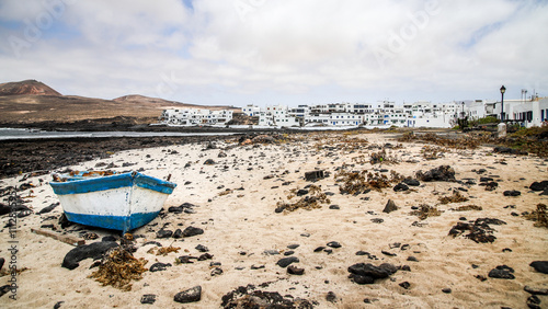 bateau en bois bleu et blanc échoué sur une plage de sable avec un village aux maisons blanches en arrière plan