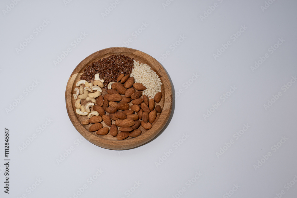 Fototapeta premium mix of nuts almonds and cashews and flax seeds and sesame seeds lie on a round wooden plate on a white background