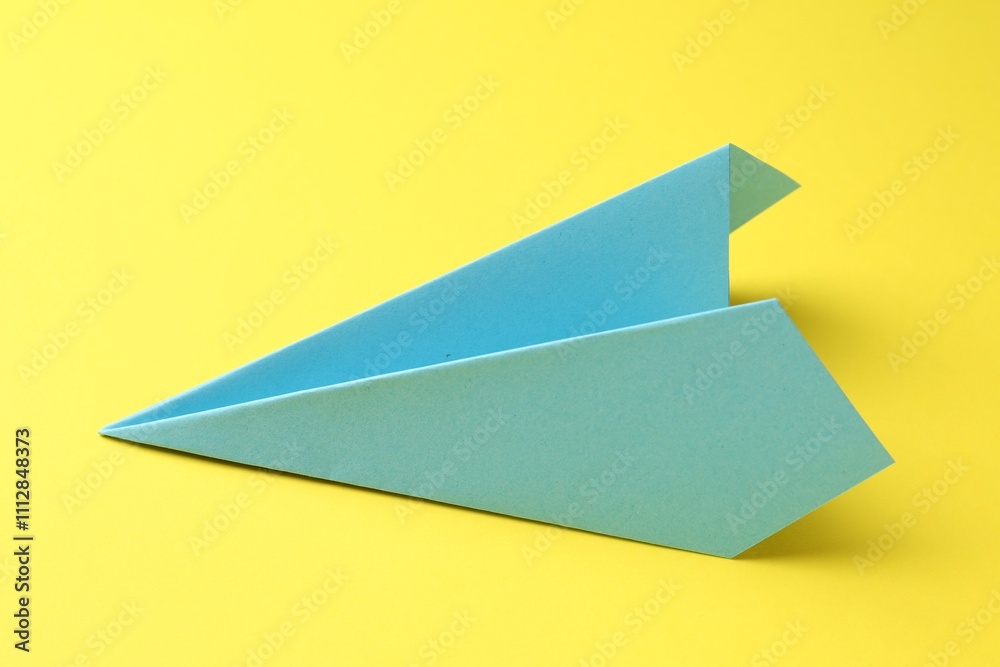 One handmade light blue paper plane on yellow background One handmade light blue paper plane on yellow background