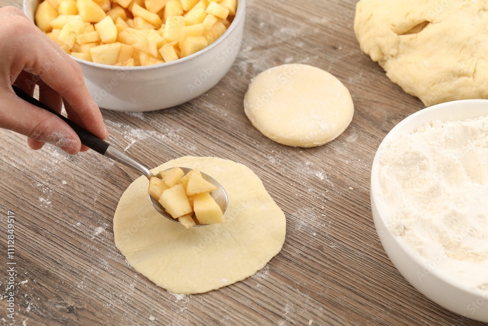 Woman making pirozhki (stuffed pastry pies) with apples at wooden table, closeup Woman making pirozhki (stuffed pastry pies) with apples at wooden table, closeup