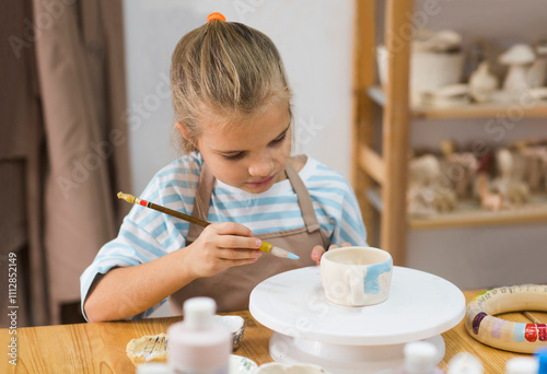 child girl paints a made clay mug pottery school. Kid sculpts clay crafts pottery school.