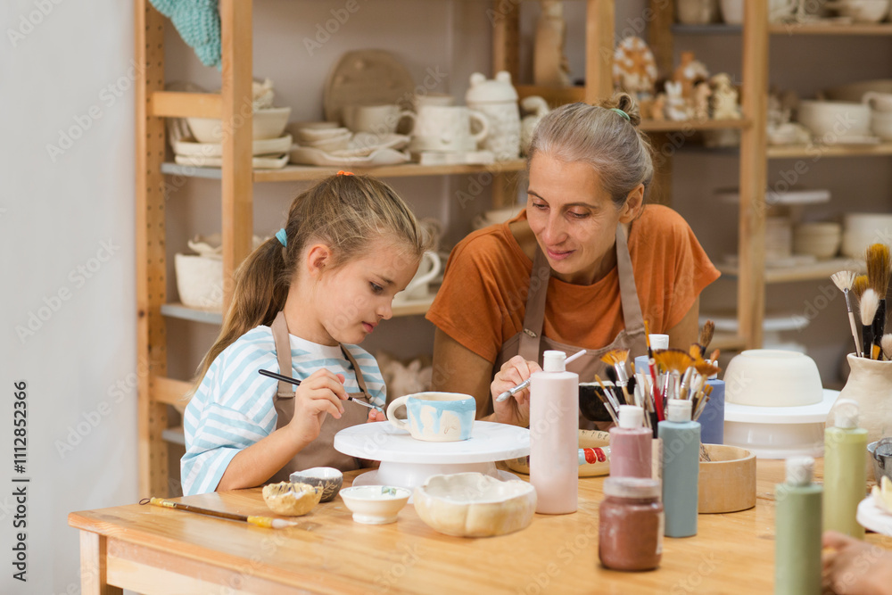 mother and child daughter paint the clay mugs they made crafts pottery school. A professional potter teaching and coaching kid making a pottery in the workshop.
mother and child daughter paint the clay mugs they made crafts pottery school. A professional potter teaching and coaching kid making a pottery in the workshop.