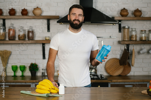 Portrait of athletic man with beard  in sportswear at the kitchen is holding shaker with whey protein or water. Healthy sporty lifestyle