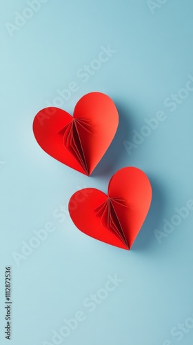 Three red paper hearts against a light blue background create a cheerful deco...