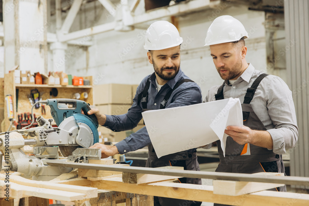 Carpenters reading blueprint and using circular saw in workshop Carpenters reading blueprint and using circular saw in workshop