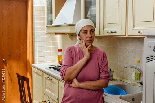 Thoughtful moroccan woman with headscarf standing in her kitchen photo