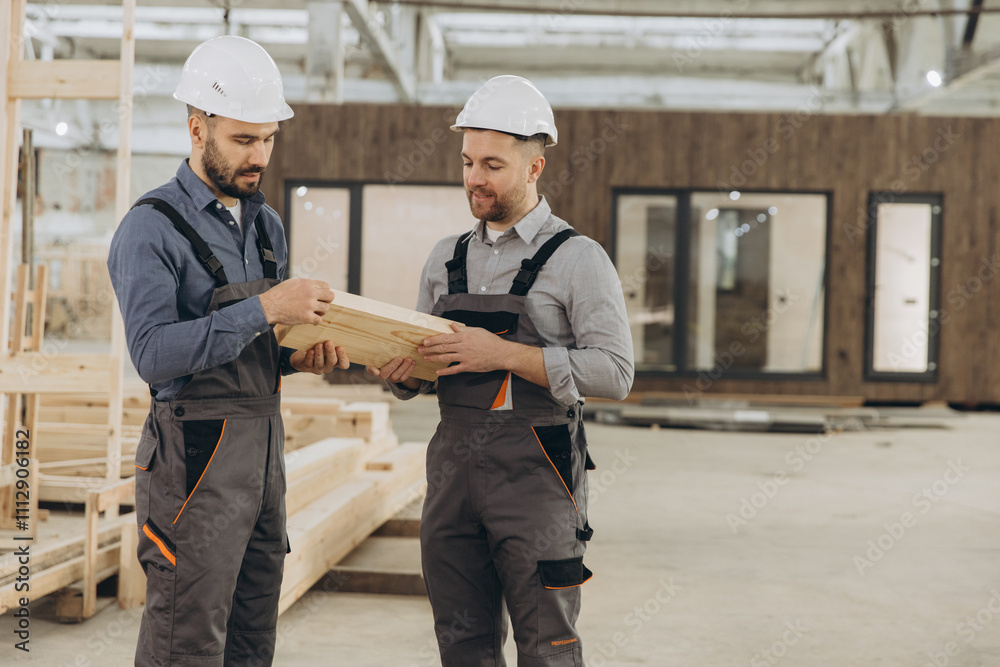Construction workers examining wooden plank in modular building factory Construction workers examining wooden plank in modular building factory
