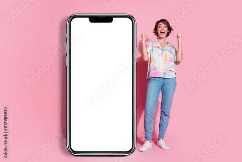 Full size photo of pretty young lady raise fists empty space smart phone screen isolated on pink color background