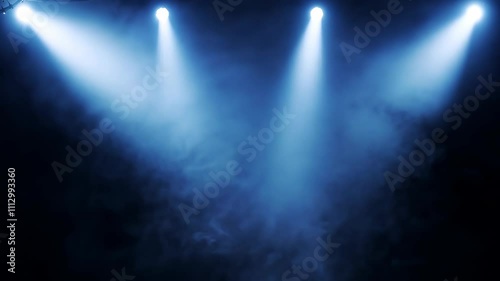 Multiple blue spotlights pierce through dark stage space, creating dramatic beams against black background filled with rising smoke.
