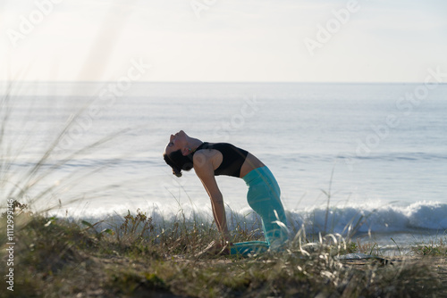 Young woman practicing ustrasana yoga pose on the beach at sunrise photo