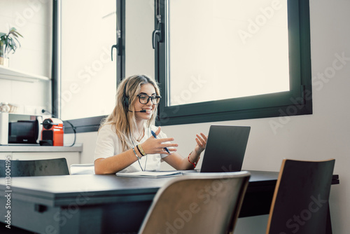 Happy millennial female in headphones watch webinar on laptop in modern office, smiling young businesswoman have fun laugh talk on video call with client or colleague use wireless Internet connection. photo