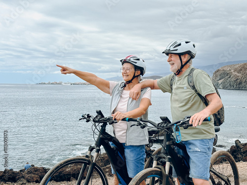 Two happy old mature people enjoying and riding bikes together to be fit and healthy outdoors. Active seniors having fun training in nature. Portrait of one old man smiling in a bike trip with wife