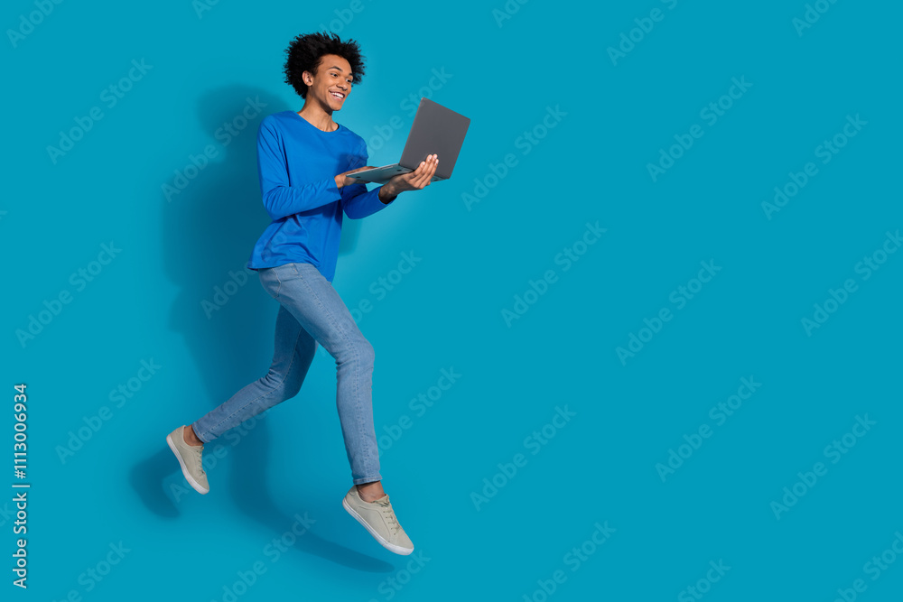Full length photo of handsome young guy running hold netbook dressed stylish garment isolated on blue color background Full length photo of handsome young guy running hold netbook dressed stylish garment isolated on blue color background
