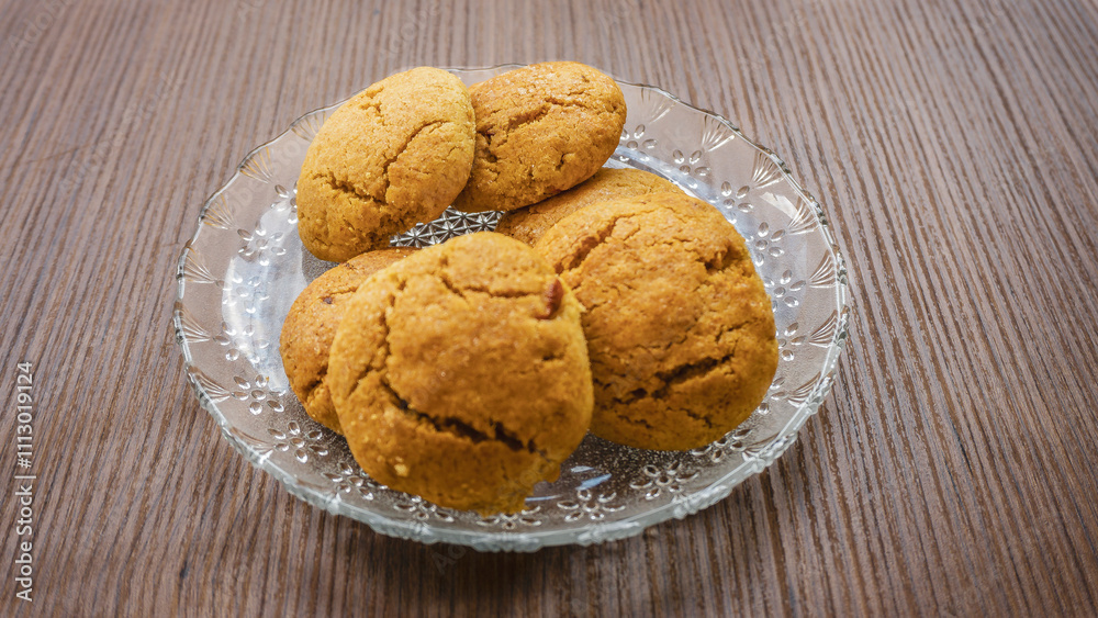 A plate of freshly baked golden-brown cookies served on a glass dish. A plate of freshly baked golden-brown cookies served on a glass dish.